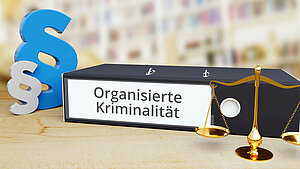 Organisierte Kriminalität – Recht/Gesetz. Ordner auf Schreibtisch mit Beschriftung neben Paragraf und Waage. Anwalt
